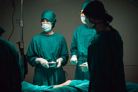 Asian Medical Team Performing Surgical Operation in Modern Operating Room. Doctors and Nurse in green uniform concentrate working in the hospital.の写真素材