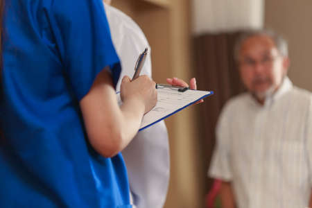 Close up Nurse hand writing the check up result from the doctor into her clipboard. Asian Doctor nurse and parent talking ing patient room.の写真素材