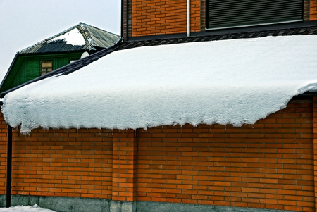 Icicles and snow on the roof above the fenceの写真素材