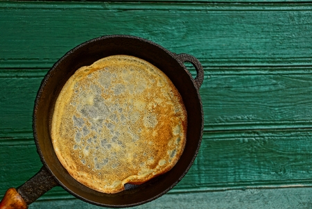 A pancake in a frying pan on a wooden wall backgroundの写真素材