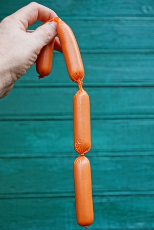 Raw sausages in a hand on a green backgroundの写真素材