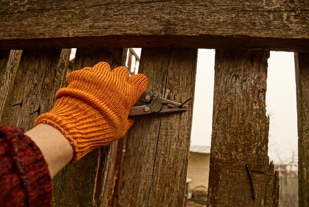 Pliers in the hand and a rusty nail in a wooden fenceの写真素材