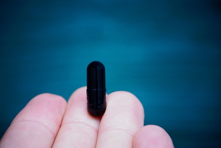 Black capsule with powder on the fingersの写真素材