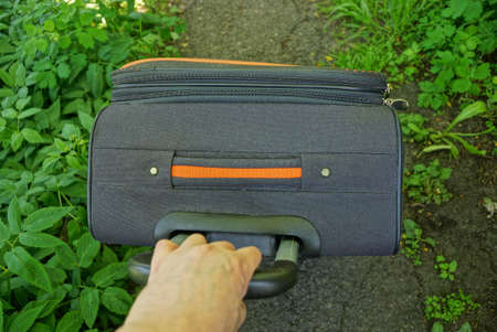 Hand pulls the handle of a large suitcase on the road