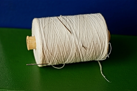 A hank of white threads and a needle on a table