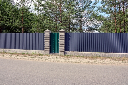 An iron fence and a green gate near asphalt roadの写真素材