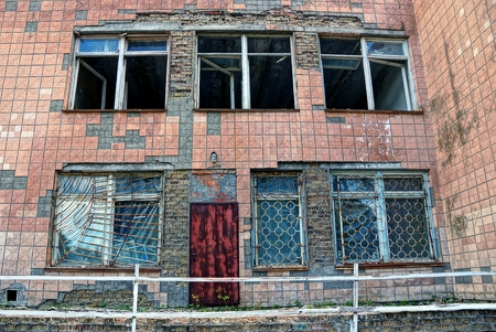Broken windows and a rusty door on the facade of an abandoned buildingの写真素材
