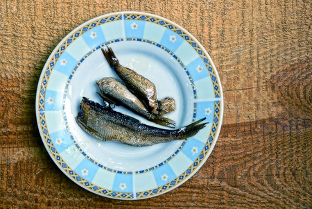 Three small fish on a white plate on a brown wooden board