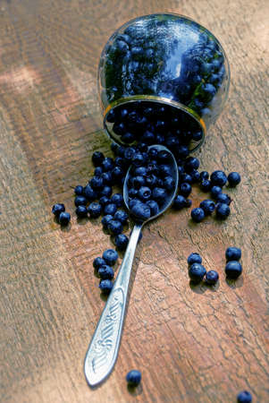 Glass glass with a spoon with sprinkled blueberries on a wooden boardの写真素材