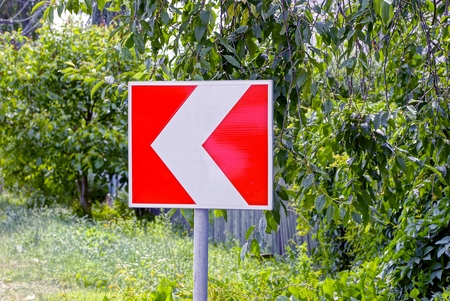 Square road sign indicating the direction of traffic against the background of greeneryの写真素材