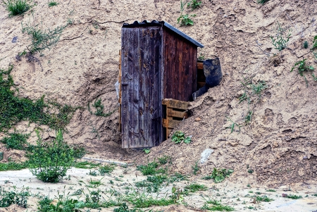 Old wooden toilet among grass and sand