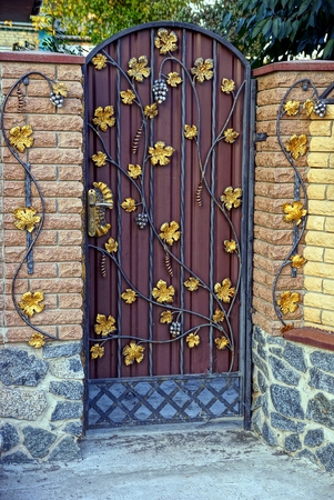 Closed iron wicket with a pattern and part of a brick wall of a fenceの写真素材