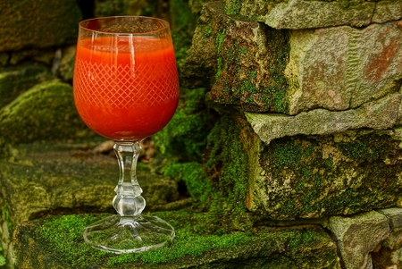 a glass with a red drink stands on bricks covered with mossの写真素材