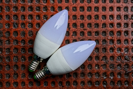 Two white led lamps lie on a muddy and damp brown sidewalk