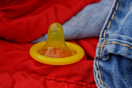 a yellow condom rests on the red-blue cloth of trousersの写真素材