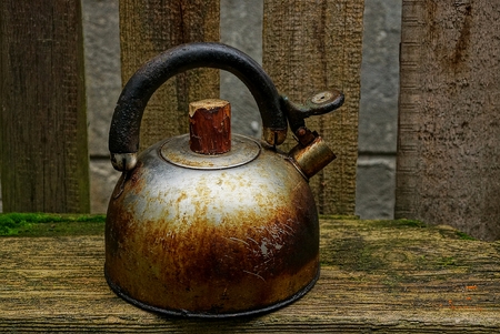 old charred iron kettle is standing by the gray wooden fence in the streetの写真素材