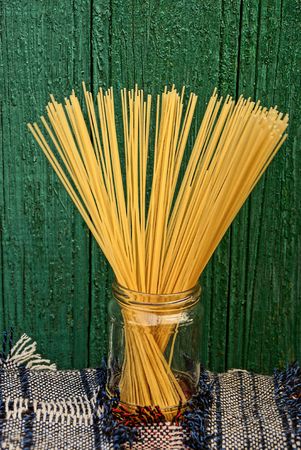 long spaghetti in a glass jar near a wooden green wallの写真素材