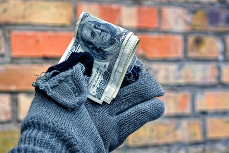 homeless man holding money in a torn glove against a brick wall backgroundの写真素材