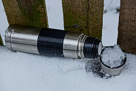 gray thermo with a cup of ice and snow near a wooden fence
