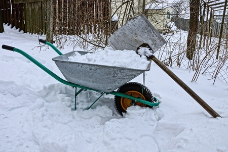 an iron wheelbarrow with snow and a shovel in a snowdriftの写真素材