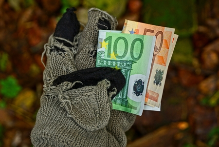 homeless man holds paper money in a tattered woolen gloveの写真素材