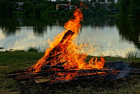 a large fire on the shore of the lake at dusk