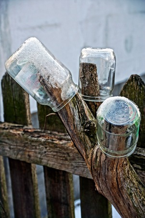 glass jars in the snow near the fenceの写真素材