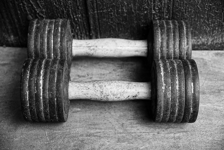 two old gray dumbbells on the floor near the wallの写真素材