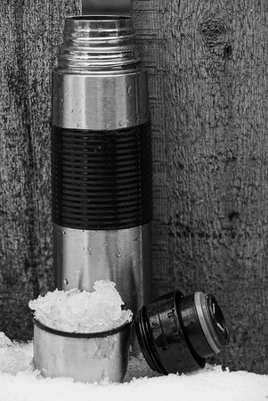 gray black thermos with a cup in the snow near the wallの写真素材