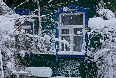 part of a wooden house with a window and branches of a bus in white snowの写真素材
