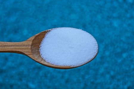 brown wooden spoon with white salt on blue background
