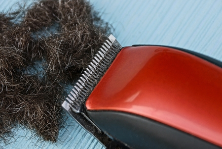 red black clipper and a bunch of hair on a blue table
