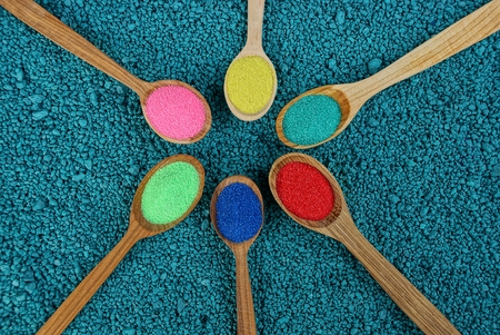 set of wooden spoons with colored sand on blue stonesの写真素材