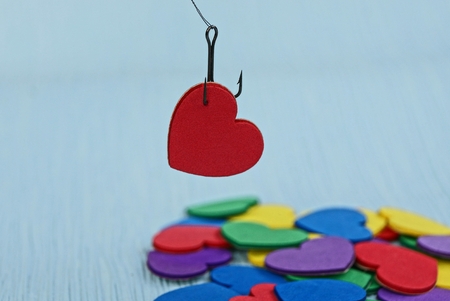 red heart on a fishing hook on a blue background over a colored heap