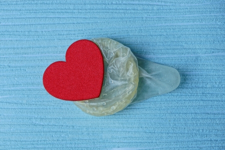 small red heart in a gray condom on a blue backgroundの写真素材