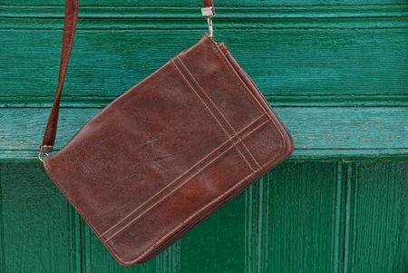 brown leather handbag hanging on a green wooden wallの写真素材