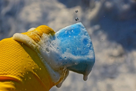 hand holds a sponge in the foam and water splashesの写真素材