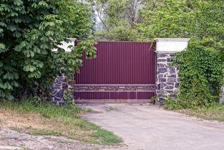 brown gate and part of the fence overgrown with green vegetation