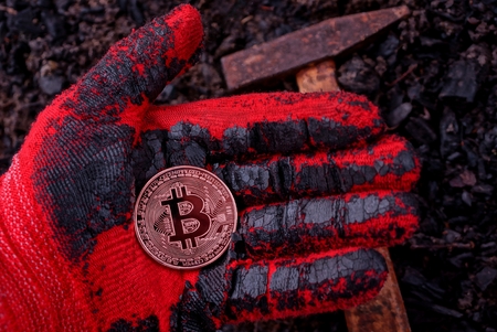 coin bitcoin lies on a gloved hand against the ground and a hammerの写真素材