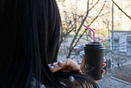 a paper glass with coffee in the hand of a girl with black hair