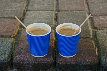 two blue paper glasses with coffee on the sidewalkの写真素材