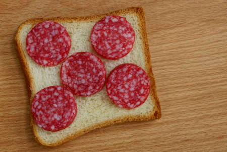 square piece of bread and sliced ??sausage salami on a brown tableの写真素材