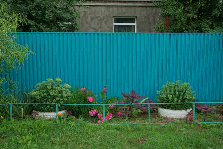 part of a blue fence made of metal in green grass and flowersの写真素材