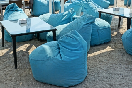 Black tables and blue puffs for sitting on the sand on the beach in a summer restaurantの写真素材