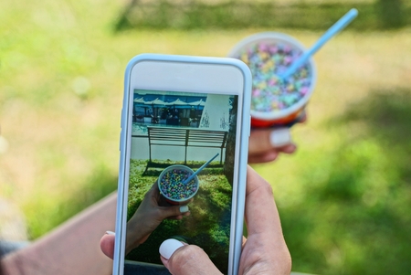 smartphone in the hands of a girl doing a photo of a colored ice cream in a cup outside in the park