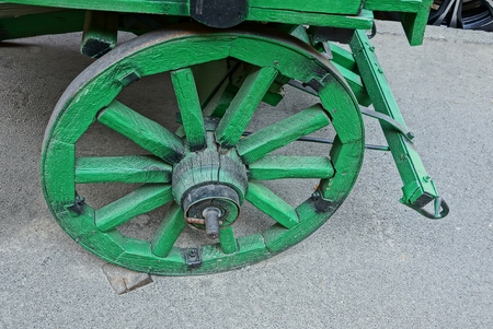 the old green wooden wheel of the wagon stands on the gray asphalt on the streetの写真素材