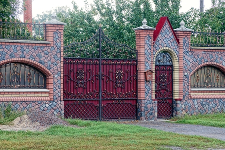 red gate and a door made of metal with a forged pattern and a stone fence in the streetのeditorial素材
