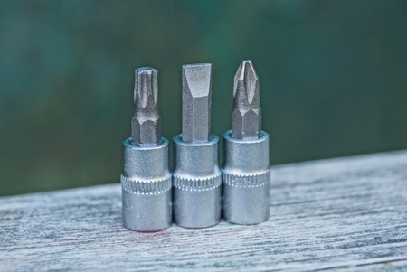 three gray metal bits for a screwdriver on a gray wooden table