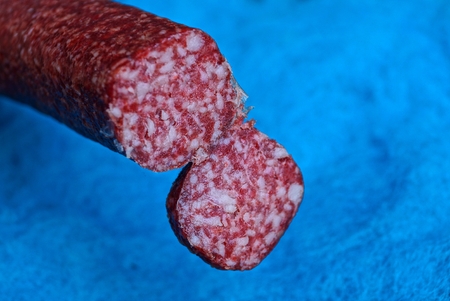 piece of red salami sausage on blue backgroundの写真素材