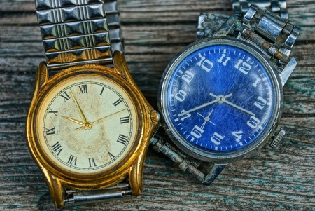 yellow and blue old shabby watch with a metal strap on a gray tableの写真素材
